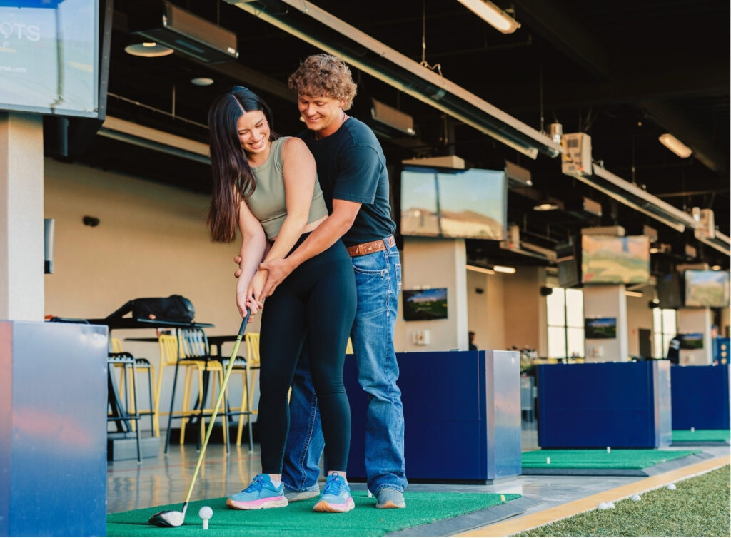 A man and woman play golf in a simulator at Crush Golf and Grill, enjoying a virtual golfing experience together.