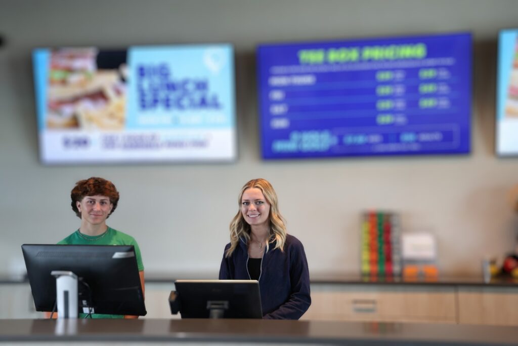 Two staff members stand behind the counter at Crush Golf and Grill, ready to assist customers.