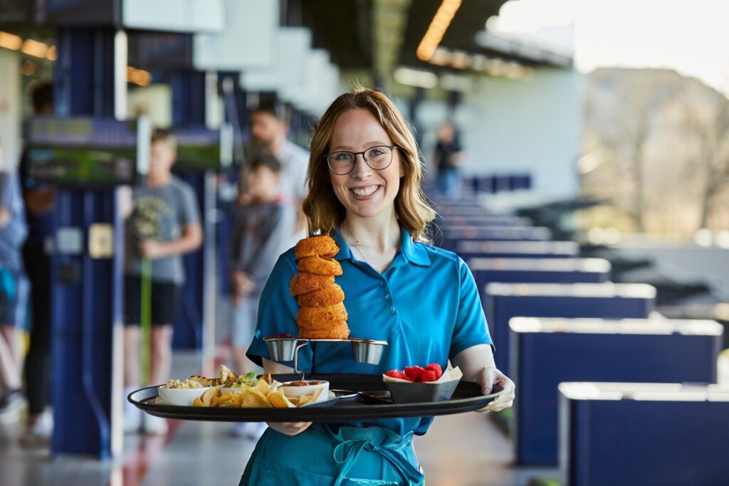 A woman in a blue shirt holds a food tray at Crush Golf and Grill, showcasing a variety of dishes.
